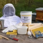 Best Beekeeping Starter Kit for Beginners: Buy Top Hive Kits 21 beekeeping starter kit with a bee suit, smoker, hive tool, gloves, frames, brush, feeder, and wooden beehives arranged outdoors on a rustic table