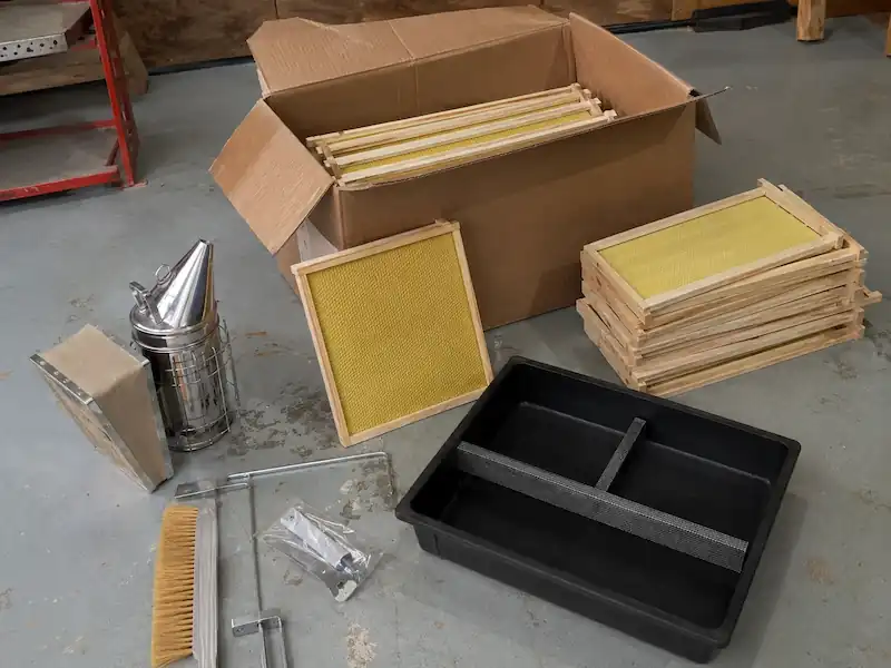 Best Beekeeping Starter Kit for Beginners: Buy Top Hive Kits 5 Beekeeping starter kit with hive tools neatly arranged on a wooden table beside a Langstroth hive
