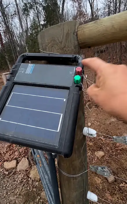 Best Electric Fence for Goats: Types, Setup & Buying Tips 6 Solar electric fence energizer mounted on a wooden post with fence wires and insulators in a wooded pasture